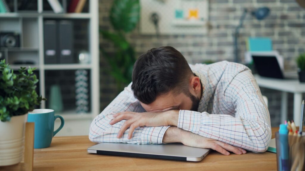 Portrait of young man employee sleeping on desk in office relaxing at work; Prince Harry and Meghan Markle Can’t Make Their Hollywood Dream Work