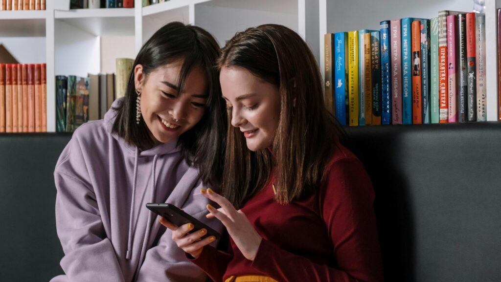 A Girl in Red Sweater Holding Her Phone while Talking to Her Friend