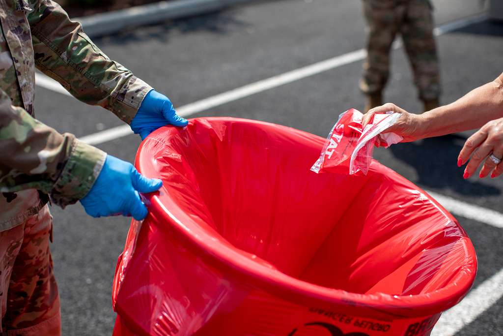 A military member wearing blue gloves while holding a red bio-hazard trash bag