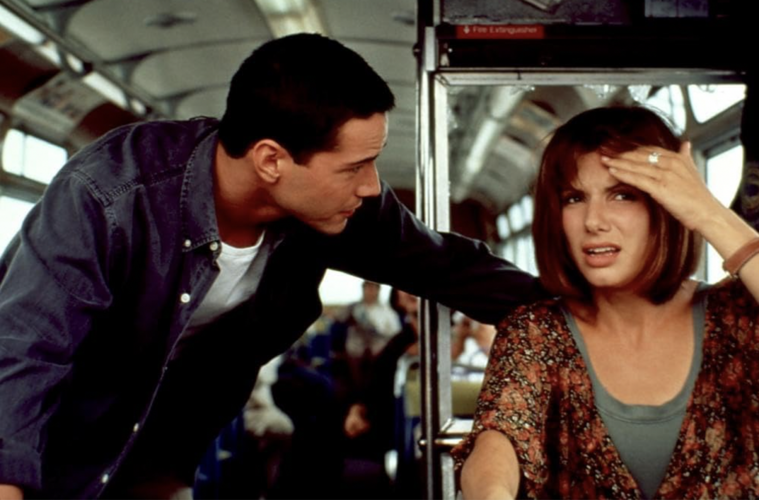 Keanu Reeves leans over Sandra bullock who is driving a bus in 1994's action film Speed