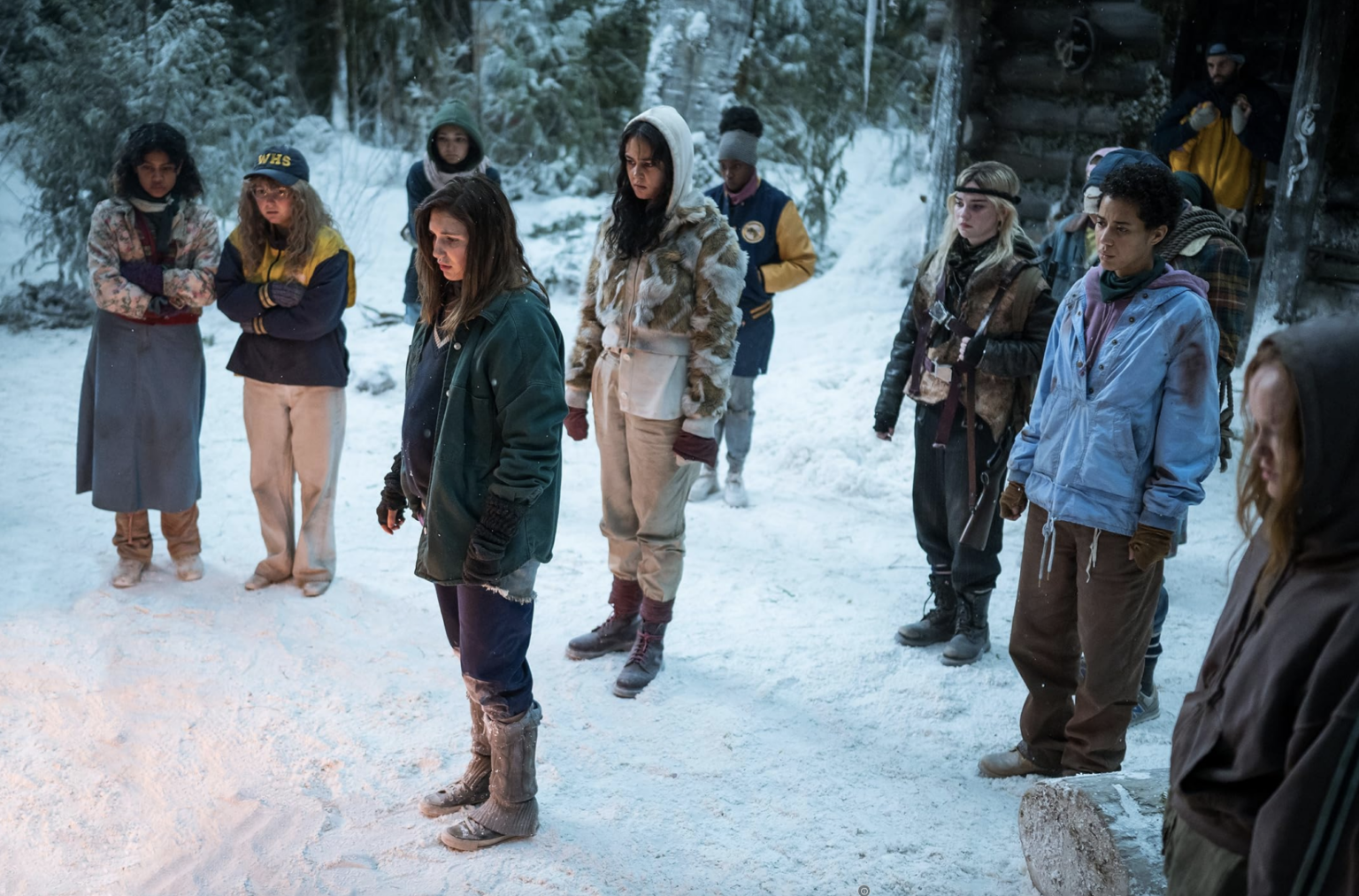 characters in a scene from Showtime's Yellowjackets standing in the snow looking at the ground solemnly