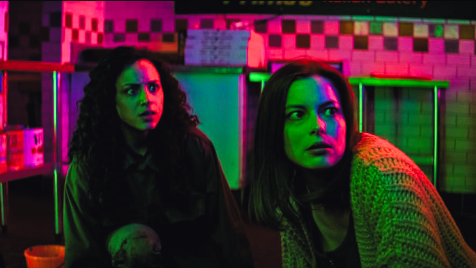 screen still of Two characters from Fear Street in multicolored lighting looking fearful