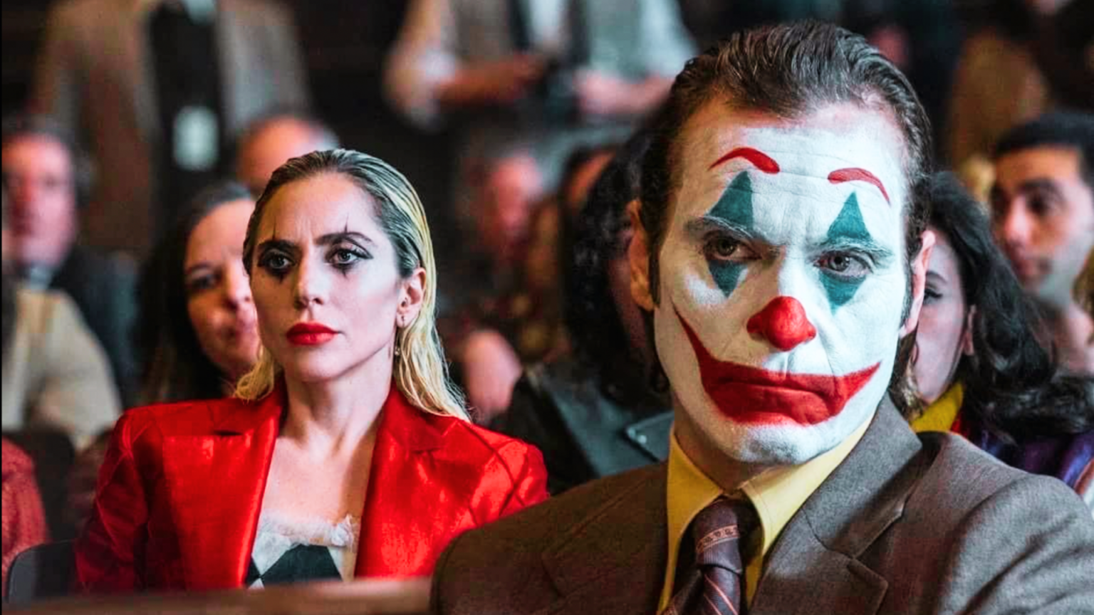 Joaquin Phoenix and Lady Gaga in the Joker sitting in a courtroom with clown makeup on