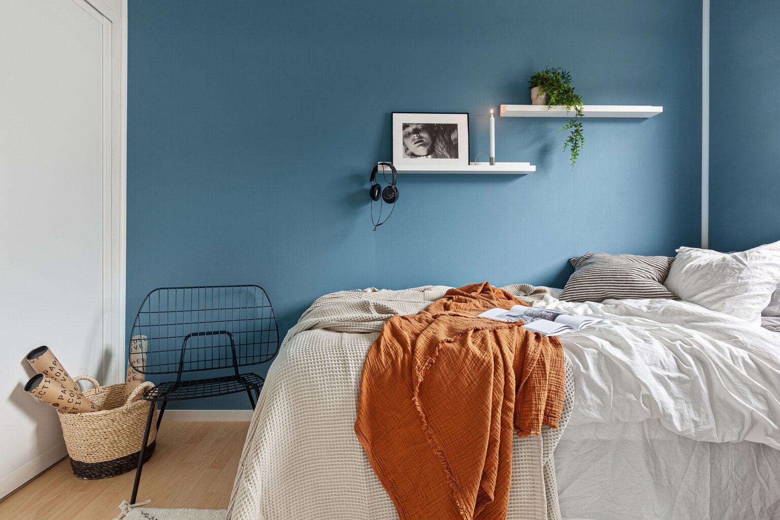 comfy bed in white linen and rust colored throw in a blue painted room