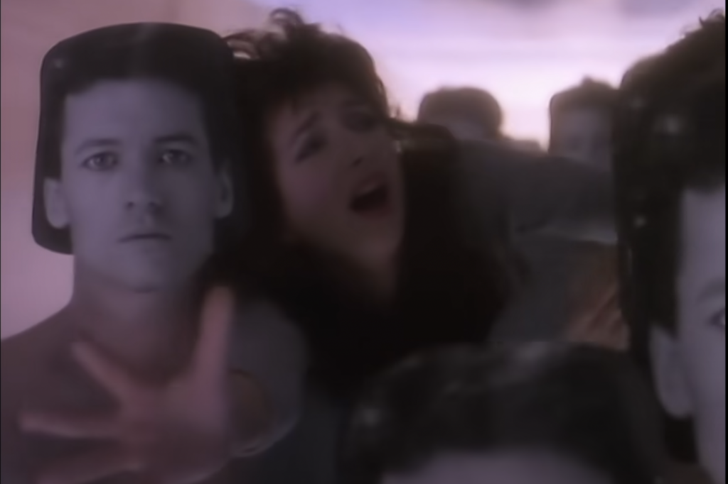 Kate Bush in Running up that hill video pushes through a hallway of figures wearing a mask of a mans face