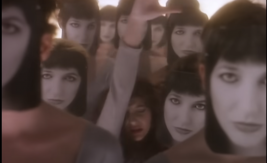 Kate Bush in Running up that hill video sinks through a hallway of figures wearing a mask of a her face face